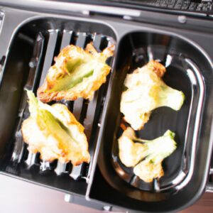 Imagem de uma couve-flor gratinada em uma Airfryer. A couve-flor é dourada e coberta com uma crosta de queijo borbulhante. A imagem é tomada de cima e o fundo da Airfryer é visível.