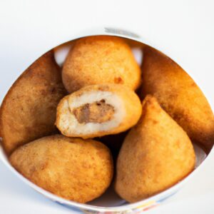 Imagem de uma coxinha de frango com batata frita em uma fritadeira AirFryer. A coxinha é marrom dourada e crocante, com uma batata frita crocante do lado. O fundo da imagem é uma mesa de madeira com um pano de prato xadrez vermelho e branco.