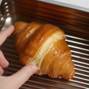 Imagem de croissants congelados dourados e crocantes cozidos em uma Airfryer, colocados em um prato com manteiga derretida ao lado.
