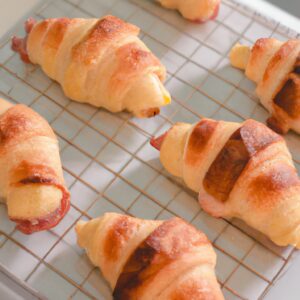 Croissants de queijo e fiambre dourados e crocantes, preparados numa Airfryer. Os croissants estão recheados com queijo derretido e fiambre fatiado, criando uma refeição deliciosa e satisfatória.