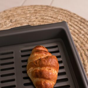 Imagem de croissants quentinhos e dourados preparados na airfryer. Eles são colocados em um prato branco e estão cercados por migalhas de pão. O fundo é uma superfície de madeira clara.