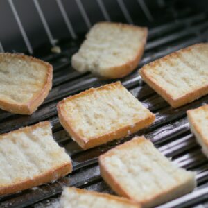 Imagem de crostinis de tapioca feitos na airfryer. Os crostinis são crocantes e dourados, cobertos com uma mistura de atum, tomate, cebola roxa e azeitonas pretas.