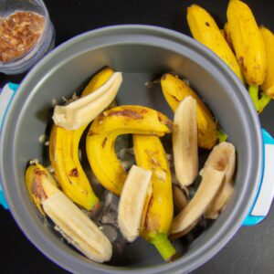Imagem de uma airfryer com uma porção de cuca de banana recém-assada dentro. A cuca está dourada e tem uma textura macia e fofa. Ao lado da airfryer, há uma tigela com os ingredientes usados para fazer a cuca, como farinha, açúcar, ovos e bananas.