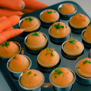 Imagem de cupcakes de cenoura fofos e dourados cozidos em uma airfryer, cobertos com um creme de queijo cremoso.