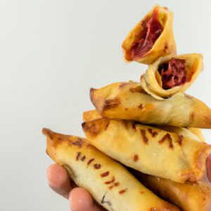 Fotografia de um enroladinho dourado crocante feito com massa de pastel cozida na airfryer. O enroladinho está cortado ao meio, revelando um recheio farto e fumegante.