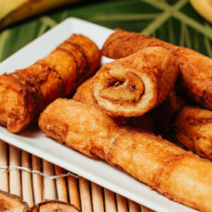 Imagem de enroladinhos de banana fritos na airfryer, polvilhados com canela. Esses enroladinhos são uma guloseima deliciosa e fácil de preparar.