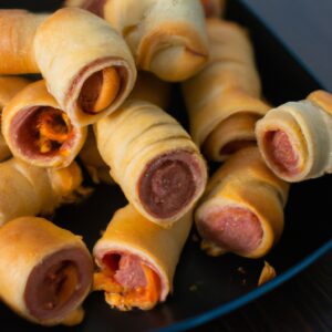 Imagem de enroladinhos de salsicha envoltos em massa de pastel, assados na Airfryer. Os enroladinhos estão dourados e crocantes, com um recheio de salsicha suculento. Eles são servidos em um prato com um molho de mostarda ao lado.