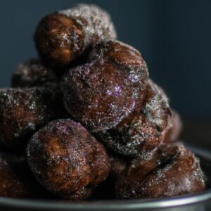 Imagem de um filé de cação assado e dourado na Airfryer, servido com limão e ervas frescas. O fundo tem uma tábua de cortar de madeira com ingredientes como pão ralado, farinha e temperos.