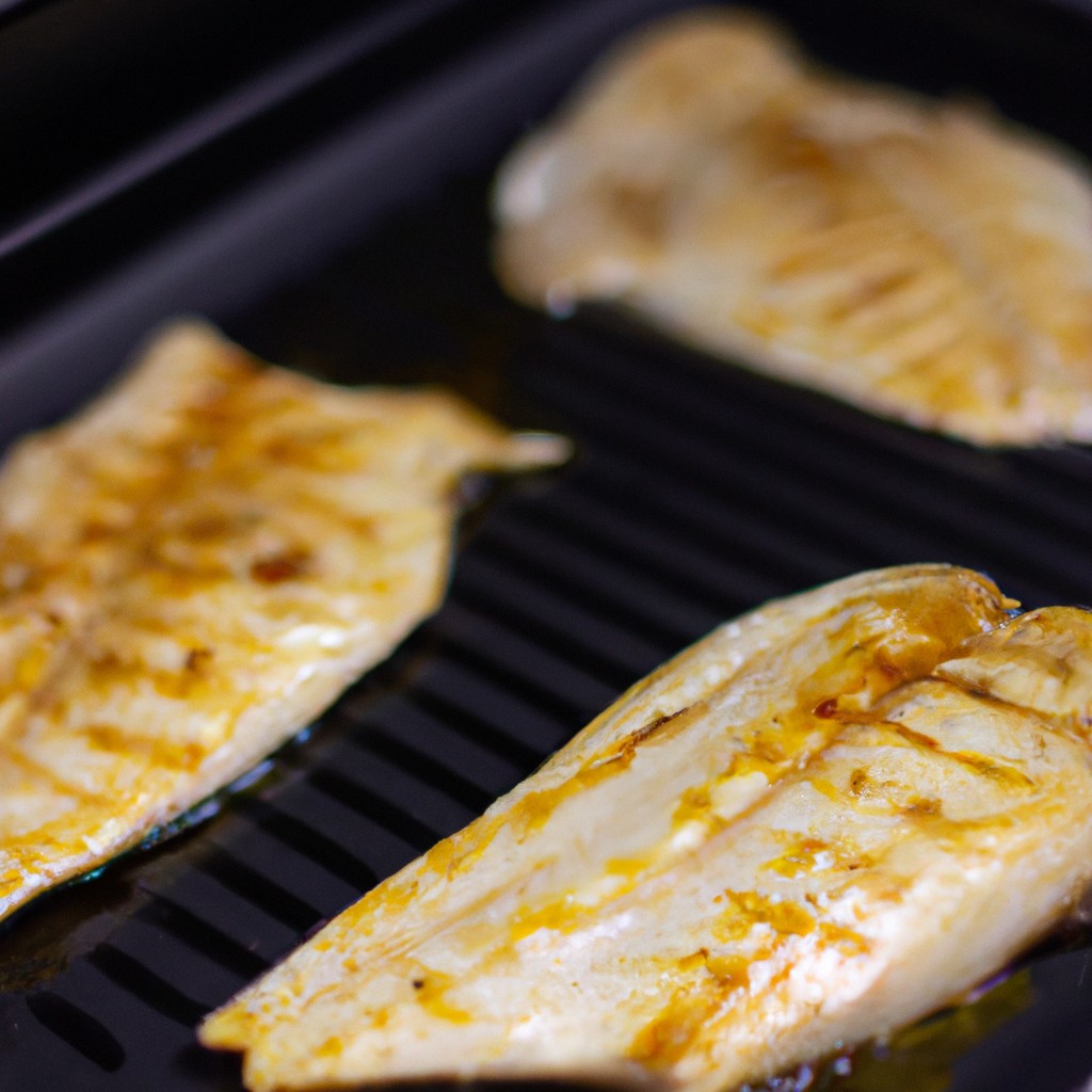 Filé de tilápia cozido no forno ou fritadeira, com pele dourada e crocante. O peixe é temperado com ervas e especiarias, e servido com fatias de limão e ervas frescas.