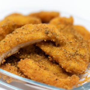 Imagem de um filé de dourada crocante e dourado cozido em uma Airfryer. O peixe é servido em um prato com rodelas de limão e ervas frescas.
