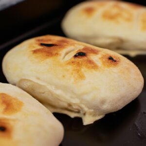 Uma foto de focaccia recheada cozida em uma Airfryer. A focaccia é quadrada, com uma crosta crocante e dourada e um interior macio e fofo. Ela é recheada com uma mistura de queijo mussarela, presunto e manjericão.
