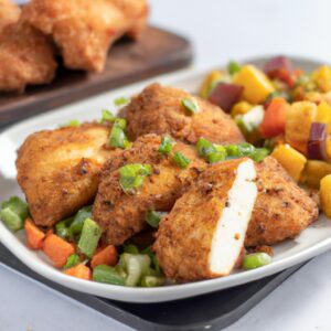 Imagem de um prato de frango com legumes assados na airfryer. O frango está dourado e crocante, e os legumes estão coloridos e tenros. A imagem mostra o contraste entre a crocância do frango e a maciez dos legumes.