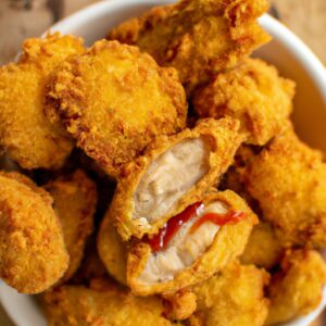 Imagem de frango empanado dourado e crocante em uma cesta da Airfryer, com fatias de limão e ervas frescas como guarnição.