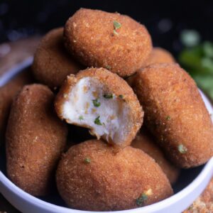 Imagem de um kibe vegano dourado e crocante cozido em uma airfryer, servido com um molho de tahine e fatias de limão.
