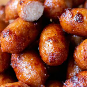 Imagem de linguiças defumadas grelhadas em uma Airfryer. As linguiças estão douradas e crocantes, com um leve toque de fumaça. Elas são servidas em um prato com fatias de pão e mostarda.