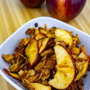 Imagem de uma maçã assada na Airfryer, servida com granola. A maçã é marrom-dourada e tem um recheio de granola crocante. A maçã está em um prato branco e o fundo é uma superfície de madeira.