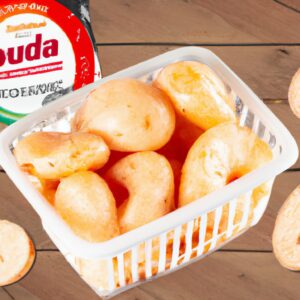 Imagem de mandioca frita crocante com queijo derretido, preparada na airfryer. A mandioca é cortada em palitos grossos e frita até dourar, enquanto o queijo é polvilhado por cima e derretido no calor da airfryer. O prato é acompanhado por um molho de pimenta.