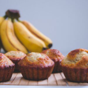 Imagem de muffins de banana recém-assados na airfryer, com gotas de chocolate por cima. Os muffins são dourados e fofos, e o fundo da assadeira é forrado com papel manteiga.