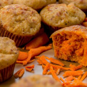 Imagem de muffins de cenoura salgados assados em uma fritadeira, servidos em um prato com cenouras raladas e ervas frescas. Os muffins são dourados e crocantes por fora, com uma textura macia e úmida por dentro.