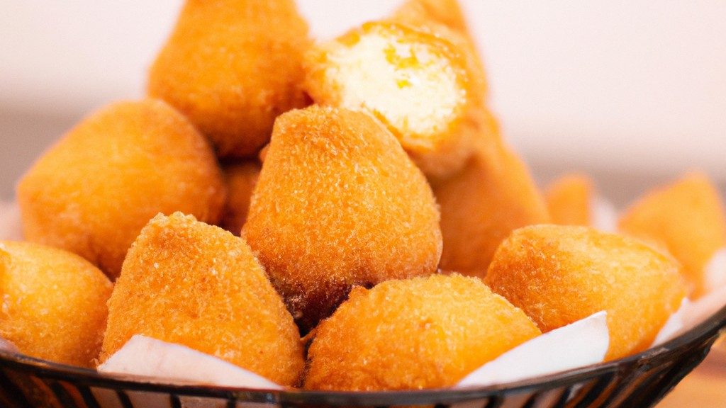 Imagem de uma tigela de pamonha cremosa feita na Airfryer, com uma colher ao lado. A pamonha tem uma cor amarela clara e uma textura cremosa, com alguns grãos de milho visíveis. O fundo é branco e a imagem está em foco.