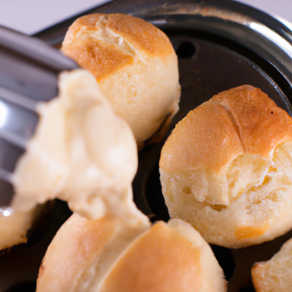 Pão Com Requeijão Na Airfryer 1 Imagem de uma cesta de Airfryer cheia de pão de queijo assados e dourados. Eles têm uma crosta crocante e um interior macio e esponjoso. Os pães de queijo são servidos em um prato com um lado de molho de tomate.