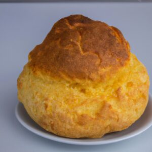 Imagem de um pão de cuscuz dourado e crocante feito na airfryer, sobre uma tábua de madeira. O pão tem uma crosta crocante e um interior macio e fofo.