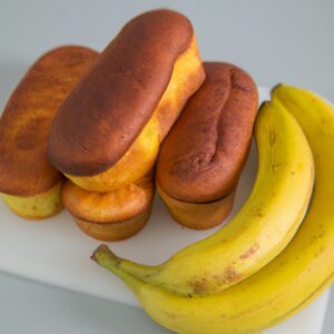 Imagem de pão de forma com banana preparado na airfryer. O pão está cortado em quadrados e tem uma cor dourada. Ele é servido em um prato branco com uma fatia de banana ao lado.