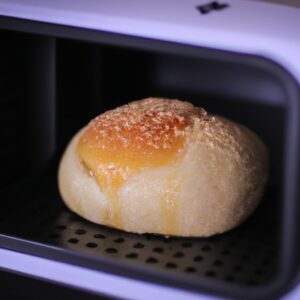 Pão de leite caseiro, preparado na airfryer, com baixo teor de carboidratos e fácil de fazer. A imagem mostra um pão dourado e crocante com uma crosta marrom clara, colocado em uma superfície de madeira. A receita é uma ótima opção para aqueles que desejam desfrutar de pão fresco e saboroso sem comprometer sua dieta low carb.