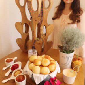 Imagem de pães de queijo crocantes e dourados em uma airfryer, acompanhados de doce de leite cremoso em uma tigela pequena.