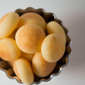 Imagem de pães de queijo de batata-doce recém-assados em uma cesta de fritadeira. Os pães de queijo são dourados e crocantes, com uma textura macia por dentro.