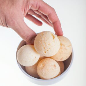 Imagem mostra uma cesta de airfryer com pães de queijo de tapioca crocantes e dourados. Os pães de queijo são feitos com uma mistura de farinha de tapioca, queijo minas padrão e outros ingredientes. Eles são assados na airfryer até ficarem inchados e dourados. A imagem mostra o interior e o exterior dos pães de queijo, destacando sua textura crocante e macia.
