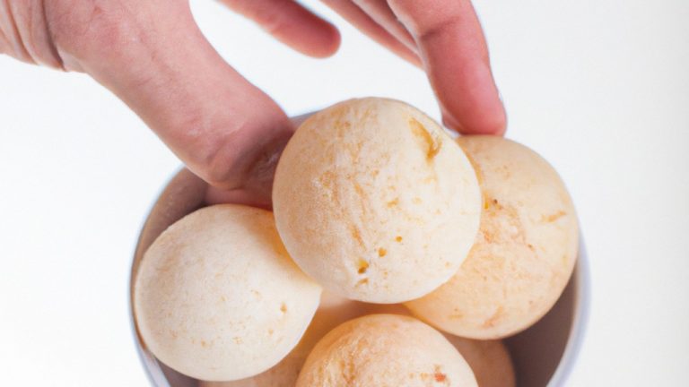Imagem mostra uma cesta de airfryer com pães de queijo de tapioca crocantes e dourados. Os pães de queijo são feitos com uma mistura de farinha de tapioca, queijo minas padrão e outros ingredientes. Eles são assados na airfryer até ficarem inchados e dourados. A imagem mostra o interior e o exterior dos pães de queijo, destacando sua textura crocante e macia.
