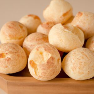 Imagem de pães de queijo dourados e crocantes em uma cesta de vime, acompanhados de um pequeno pote de mel.