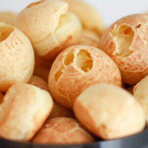 Imagem mostra uma cesta de air fryer contendo vários pães de queijo dourados e crocantes. Esses pães de queijo são uma opção leve e saborosa, feita com ingredientes saudáveis e sem glúten.
