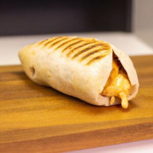 Imagem de um pão pita aberto ao meio e recheado com fatias de frango grelhado, tomate picado, cebola roxa picada, alface picada e molho de iogurte. O pão pita está assado numa Airfryer e tem um aspecto dourado e crocante.