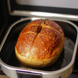 Uma imagem de pão vegano recém-assado em uma Airfryer. O pão é redondo, com uma crosta dourada e uma textura fofa. É colocado em uma cesta de metal dentro da Airfryer.