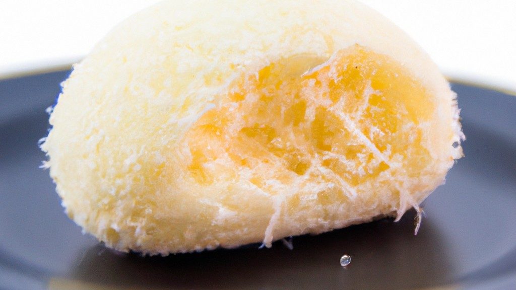 Imagem de um pãozinho de tapioca com queijo. O pãozinho é redondo e dourado, com uma textura crocante e um recheio cremoso de queijo.