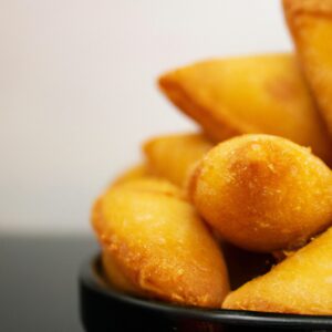 Imagem de pastéis de queijo assados na Airfryer, com uma crosta dourada e crocante. Eles estão dispostos em um prato branco, com uma tigela de molho ao lado.