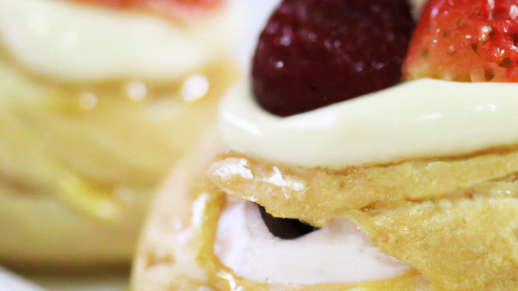 Uma imagem aérea de uma Pavlova preparada na Airfryer. A Pavlova é uma sobremesa crocante por fora e macia por dentro, coberta com chantilly e frutas vermelhas frescas. O fundo é branco e as bordas da Pavlova são douradas.