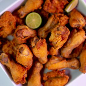 Imagem de peito de frango crocante cozido em uma airfryer em cima de uma tábua de madeira, guarnecido com ervas frescas.