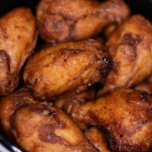Uma foto de um peito de frango empanado frito na airfryer. O frango é dourado e crocante por fora e suculento e macio por dentro. Ele está disposto em uma cesta de airfryer.