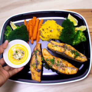 Imagem de um prato com peixe cozido e vegetais, incluindo brócolis, cenoura e cebola. O peixe está coberto por uma crosta dourada e crocante, e os vegetais estão assados e caramelizados. O prato é servido com um molho de limão ao lado.