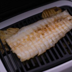 Imagem de uma posta de bacalhau assada na Airfryer. O peixe está dourado e crocante por fora, e branco e escamoso por dentro. É servido com um limão cortado ao lado.