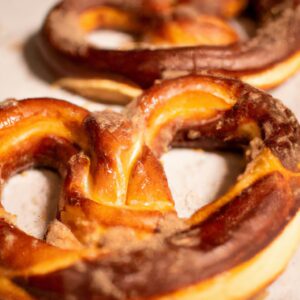 Uma fotografia de pretzels dourados e crocantes cozidos em uma Airfryer. Os pretzels têm uma crosta salgada e um interior macio e mastigável. Eles estão dispostos em uma cesta de arame com um pano de prato por baixo.