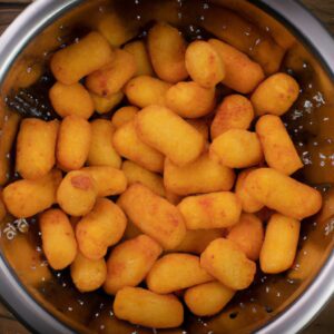 Imagem de queijo coalho frito na Airfryer. O queijo é dourado e crocante por fora, e macio e derretido por dentro. Ele está cortado em pedaços e servido com um molho de tomate.