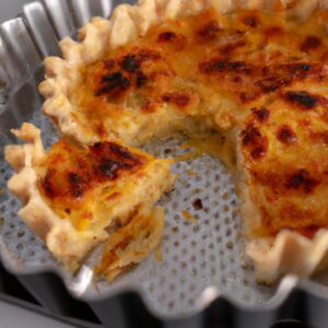 Imagem de uma quiche recém-assada em uma assadeira de ar. A quiche tem uma crosta dourada e um recheio cremoso com vegetais coloridos.