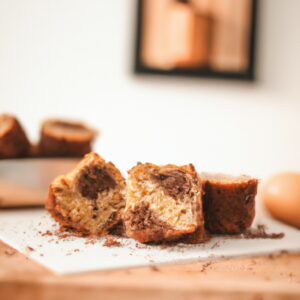Imagem de um bolinho de banana com nozes e chocolate assado em uma airfryer. O bolinho é marrom dourado e tem uma crosta crocante. No interior, o bolinho é úmido e fofo, com pedaços de banana, nozes e chocolate. O bolinho é servido em um prato com uma colher ao lado.