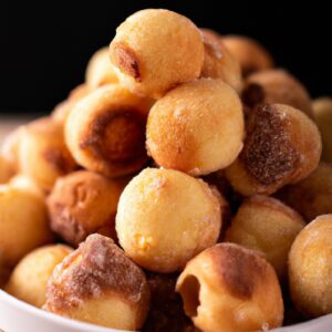 Imagem de bolinhos de chuva dourados e crocantes cozidos na airfryer, com gotas de açúcar cristalizado por cima.