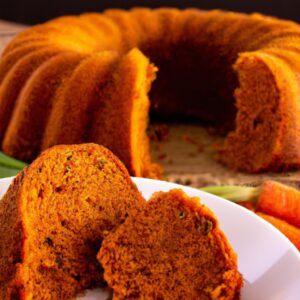 Uma foto de um bolo de cenoura redondo e dourado em uma panela preta dentro de uma Airfryer. O bolo é coberto com cobertura de cream cheese e cenouras raladas.