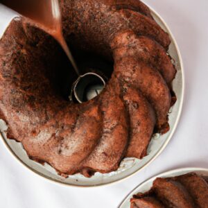 Imagem de um bolo de chocolate assado em uma airfryer. O bolo é coberto com cobertura de chocolate e tem uma colher ao lado.